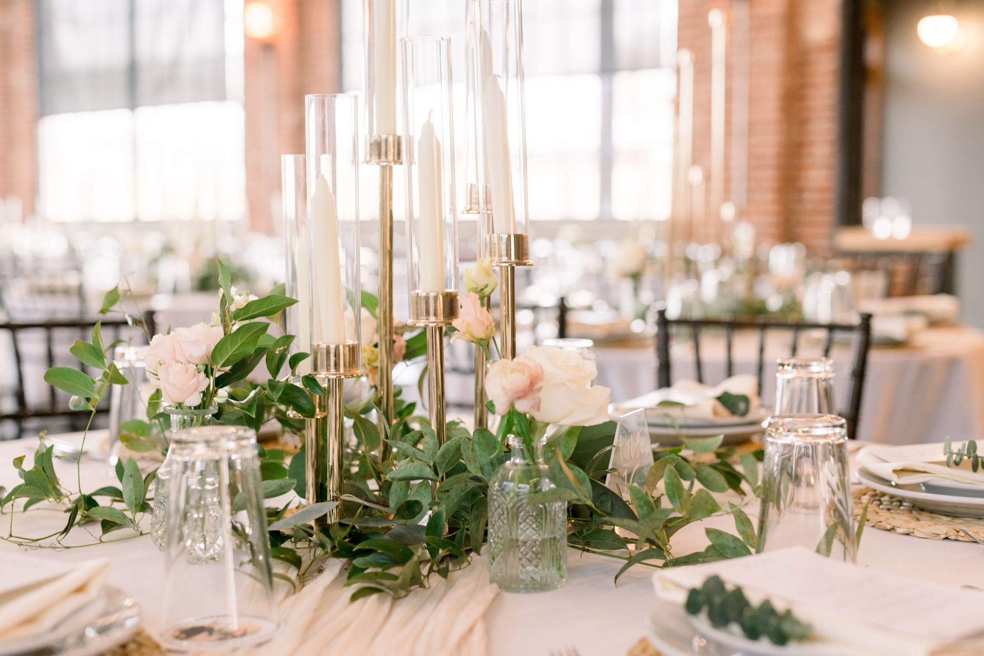 A beautiful wedding reception table decorated with greenery, simple flowers in small vases, and tall candlesticks